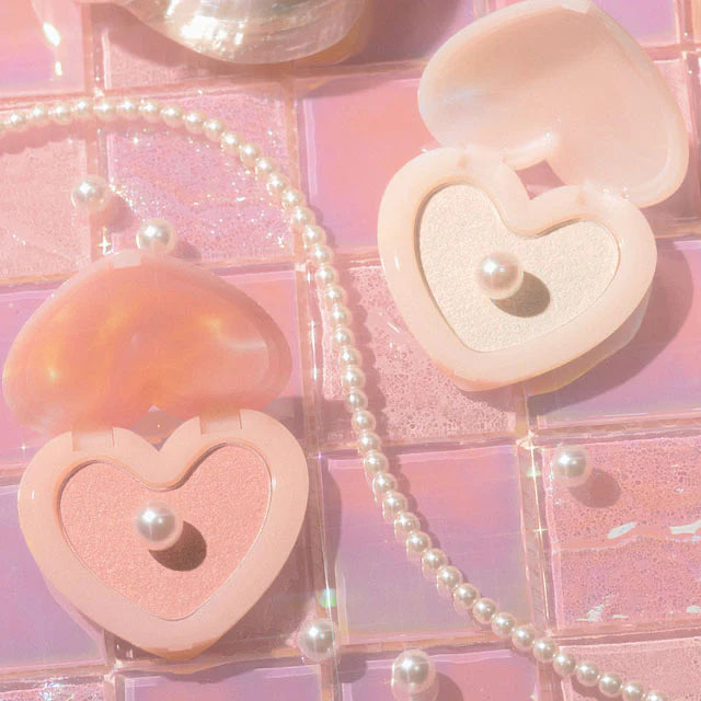 LILYBYRED Love Beam Glow Veil heart-shaped compact with shimmering shades and decorative pearls on a pink background.