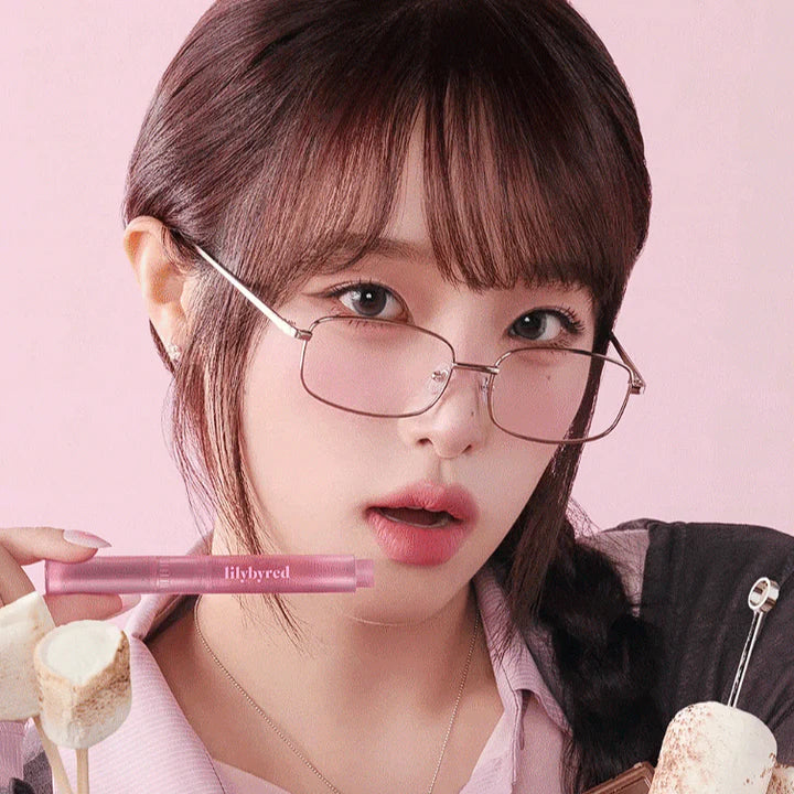 Young woman holding LILYBYRED Milky Blur Fondue Bar makeup product against a pink background.