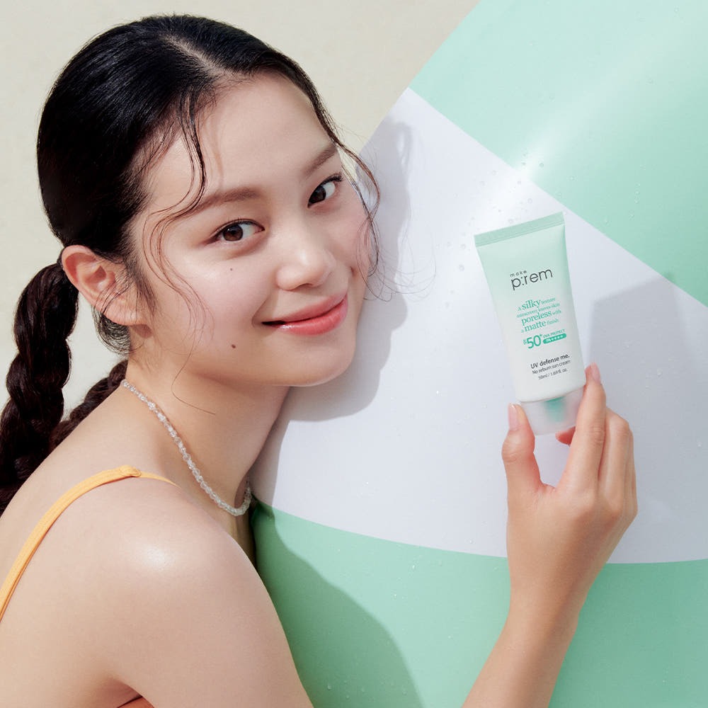 Woman holding MAKE P:REM UV Defense Me No-Sebum Sunscreen 50ml by a poolside.