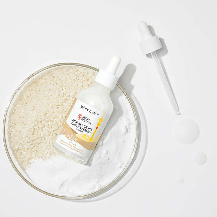 MARY & MAY Rice Niacin 10% triple Vitamin Serum with dropper and rice in background.