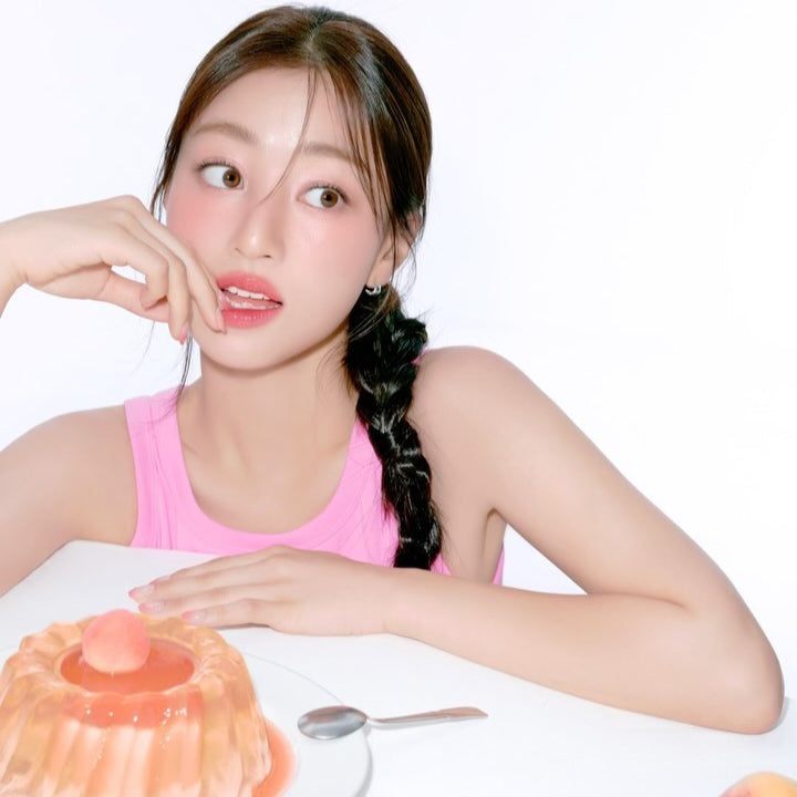 Woman wearing MILK TOUCH Jelly Fit Tinted Glow Tint with pink jelly dessert in foreground, highlighting natural, glowing makeup look.