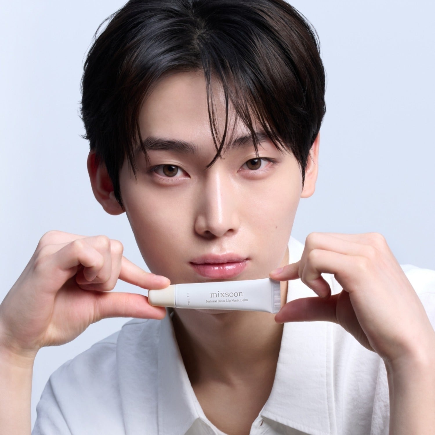 Person holding MIXSOON Natural Bean Lip Mask bean in a tube up to their face, showcasing skincare product.