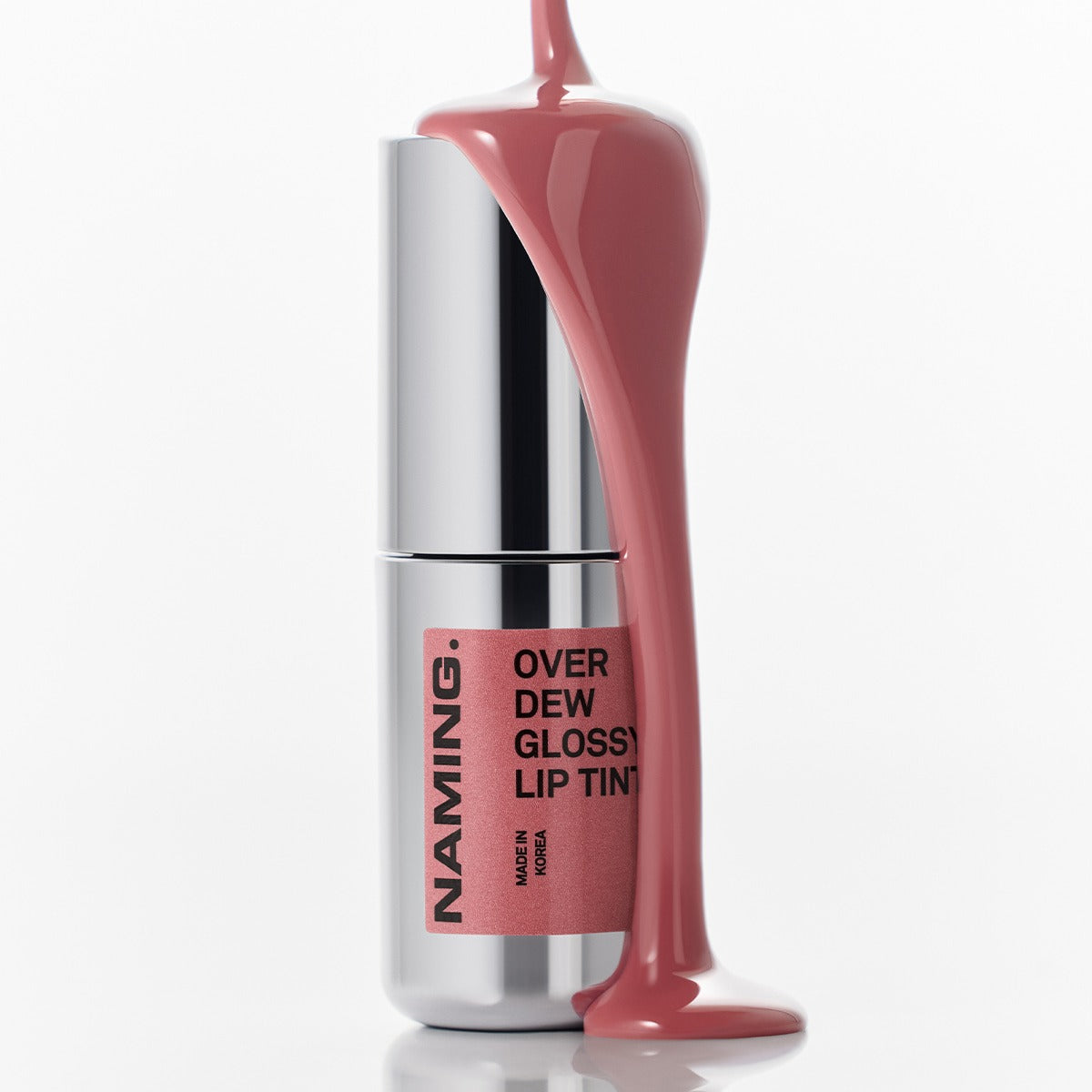 NAMING Overdew Glossy Lip Tint with pink tint flowing over silver tube, highlighting the product's shiny and sleek design.