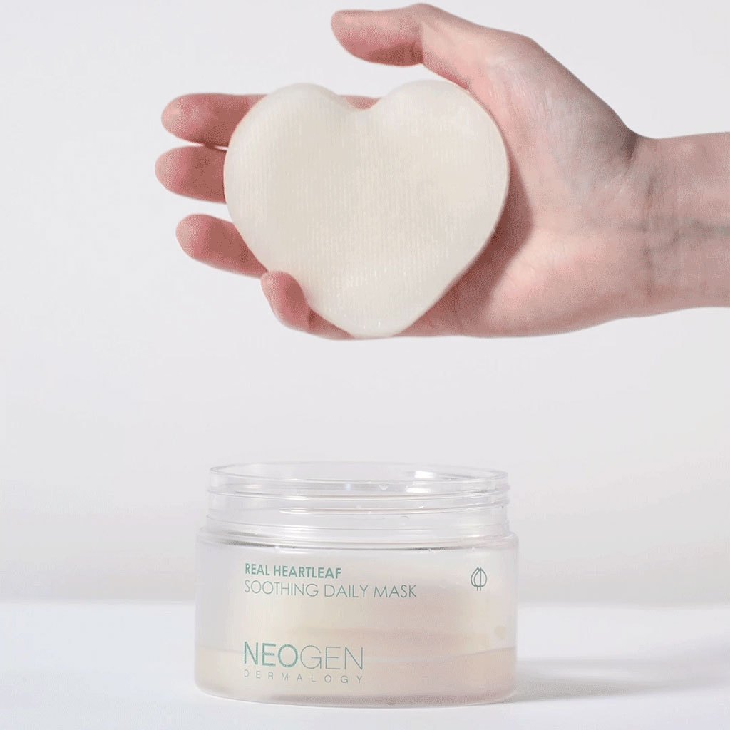 Hand holding NEOGEN Real Heartleaf Soothing Daily Mask 40 Sheets above open jar, showcasing heart-shaped pad for skincare.