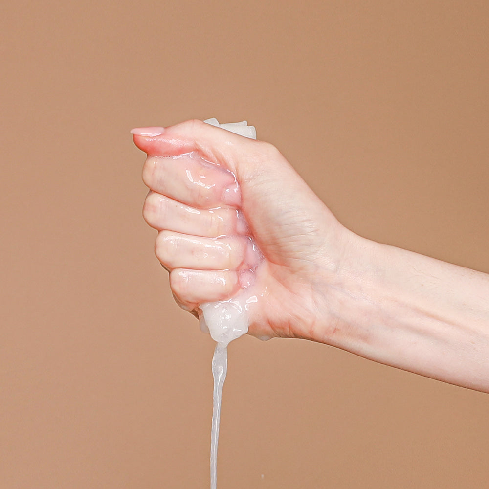 Hand squeezing liquid from NEOGEN Real Heartleaf Soothing Mask 5 Packs, demonstrating product texture on a beige background.
