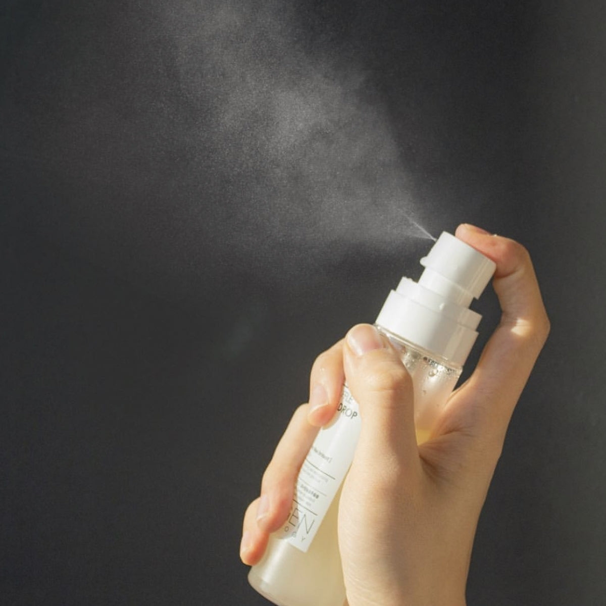 Hand holding and spraying NEOGEN White Truffle Ampoule Drop Mist 80ml against a dark background.