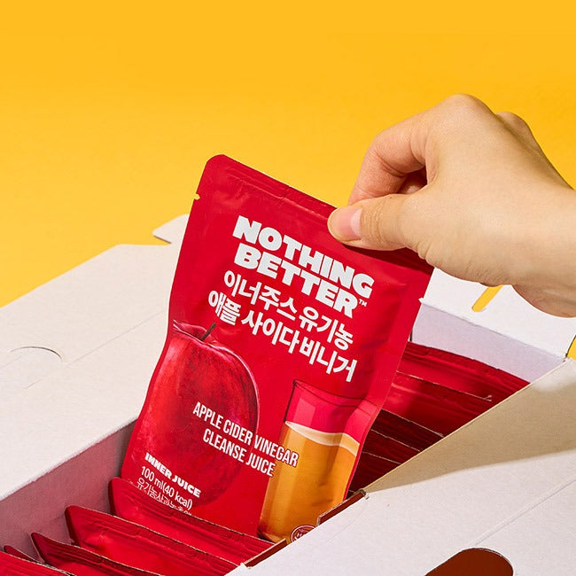 A hand holding NOTHING BETTER Inner Juice Apple Cider Vinegar Cleanse Juice (X24) packet above an open box filled with packets.