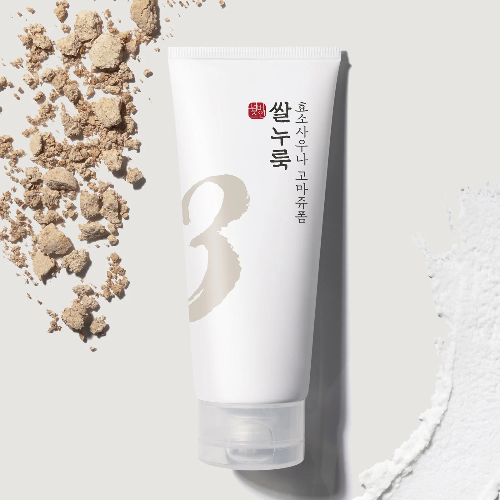 NUMBUZIN No.3 Rice Yeast Enzyme Suana Gommage Foam 170ml with textured background of rice and enzyme powder on a gray surface.