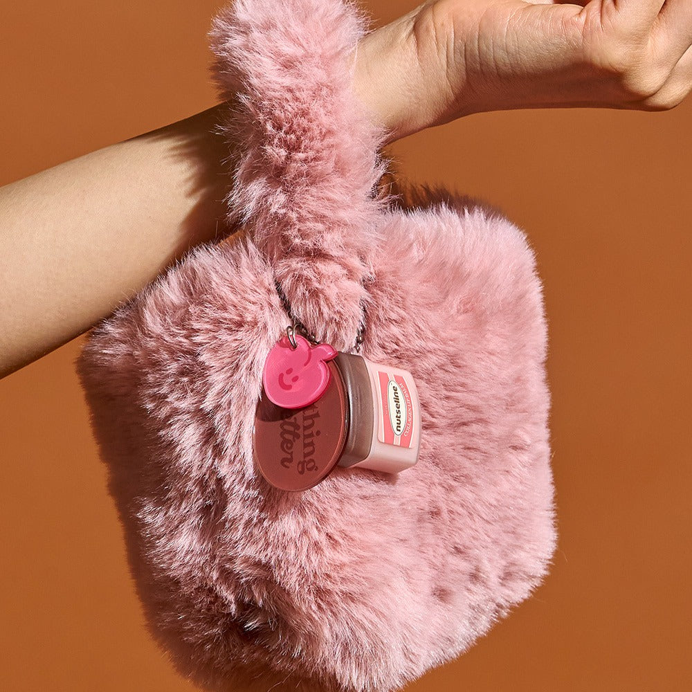 NUTSELINE Super Nut Collagen Keyring Lip Balm 11ml hanging on a pink fluffy bag held by a hand.