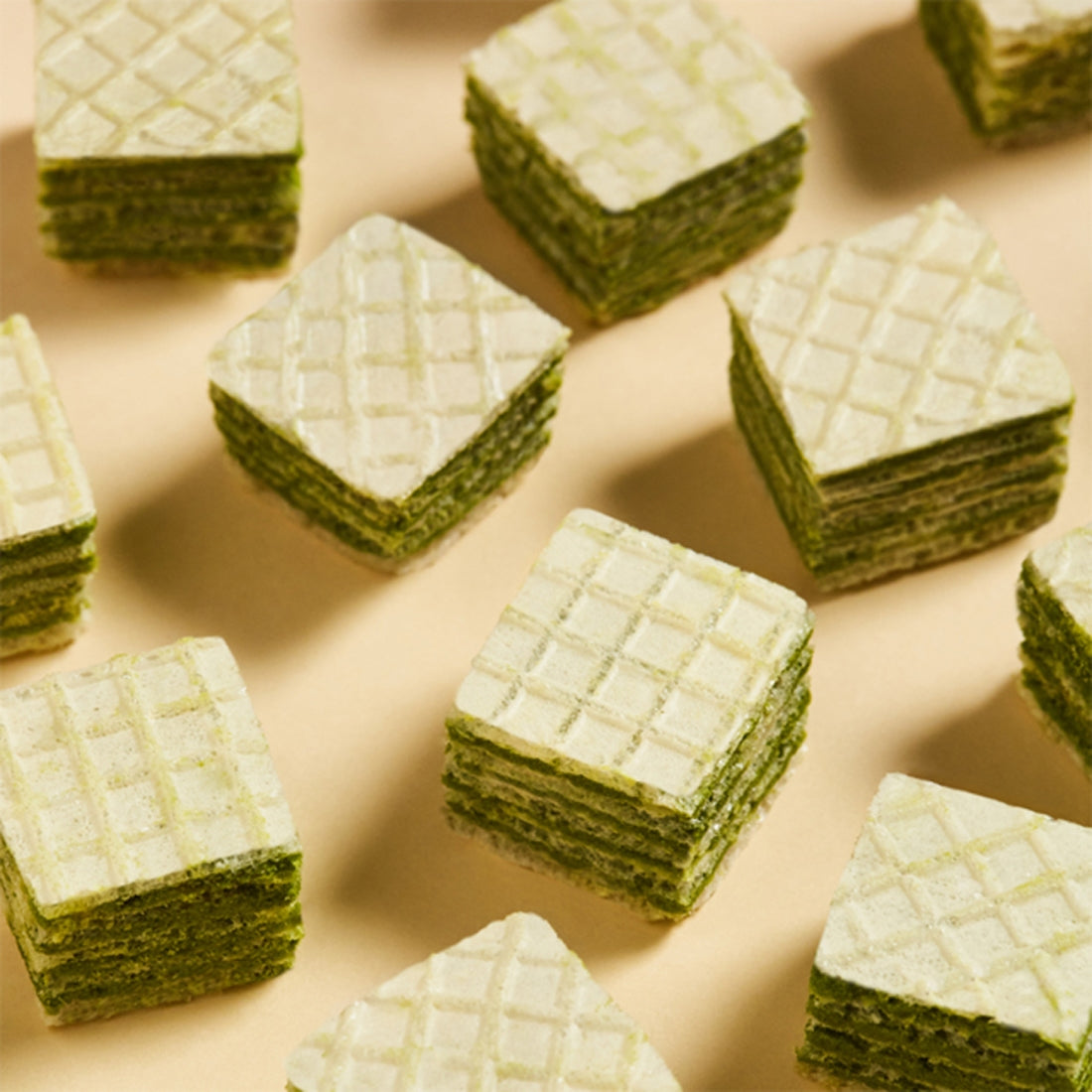 OSULLOC Green Tea Wafers 100g arranged in a grid pattern on a beige surface, showcasing layers and texture.