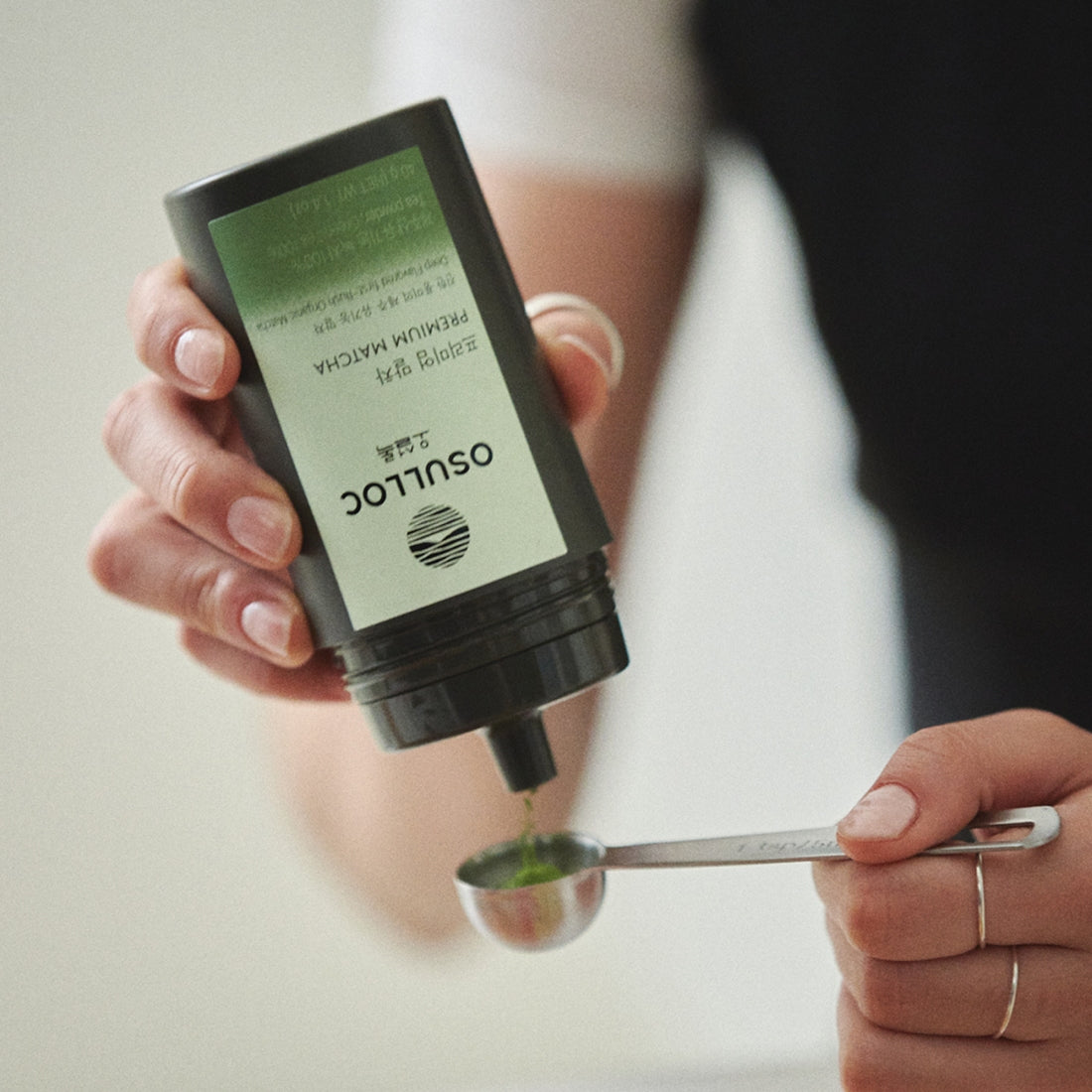 Person pouring OSULLOC Premium Matcha 40g into a measuring spoon, highlighting the premium quality of the matcha tea powder.