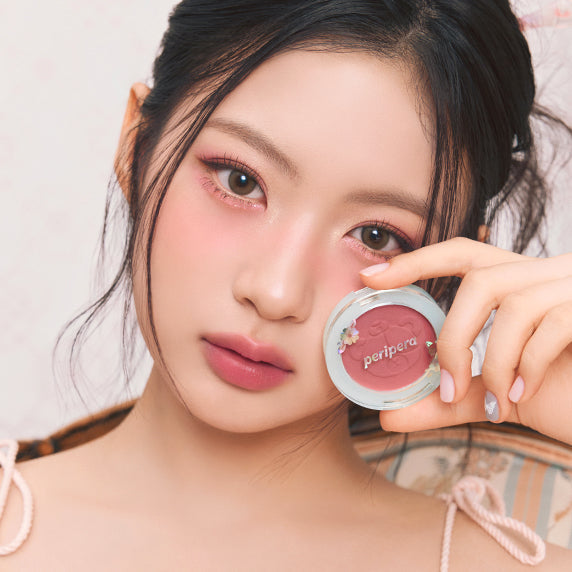 Woman holding PERIPERA Pure Blushed Sunshine Cheek, showcasing rosy makeup look.