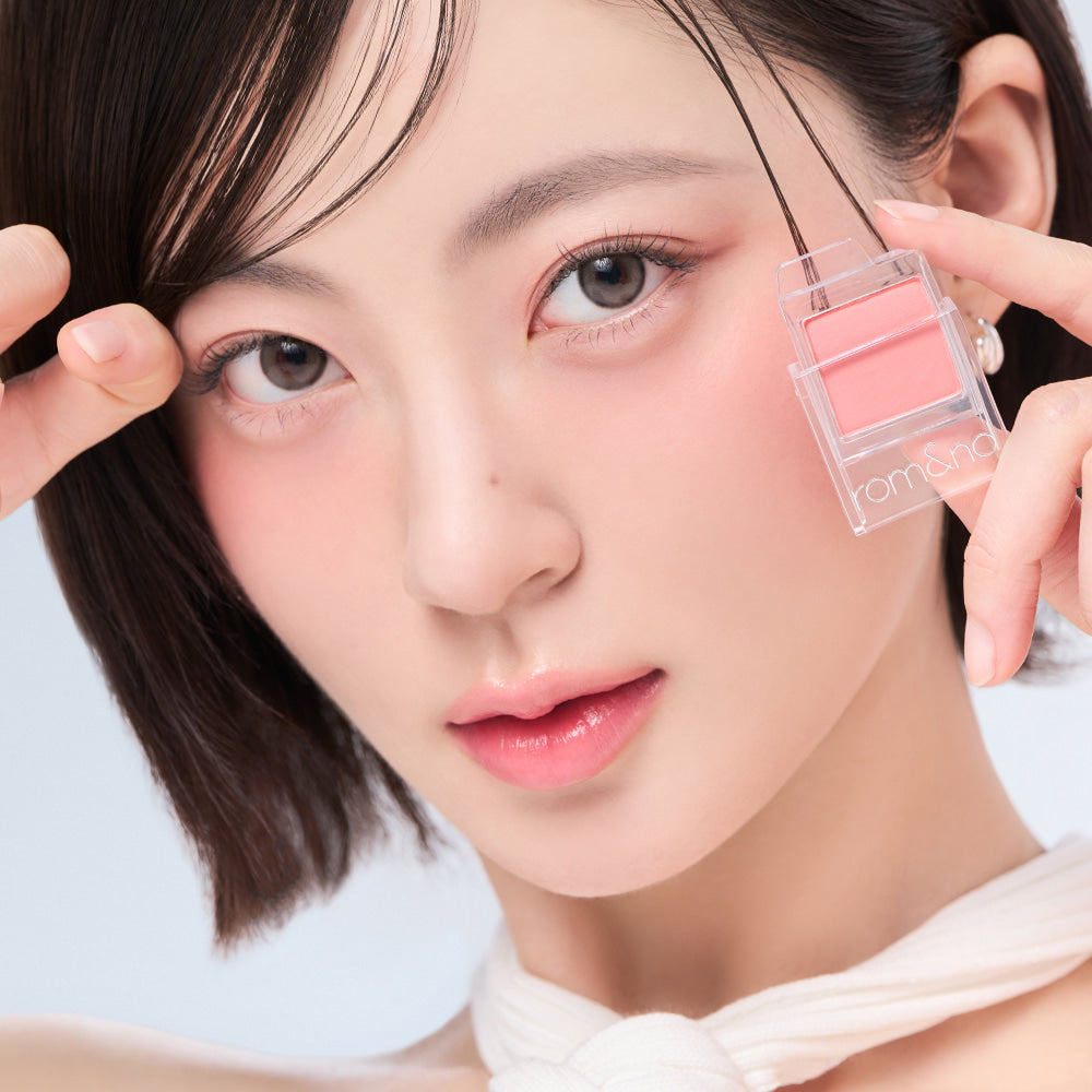 Woman holding ROMAND Slide In Single blush compact near her face, highlighting natural makeup look