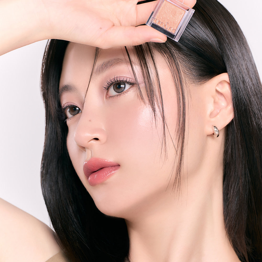 Person holding ROMAND Slide In Single makeup product near their face, showcasing vibrant cosmetic color on smooth skin.