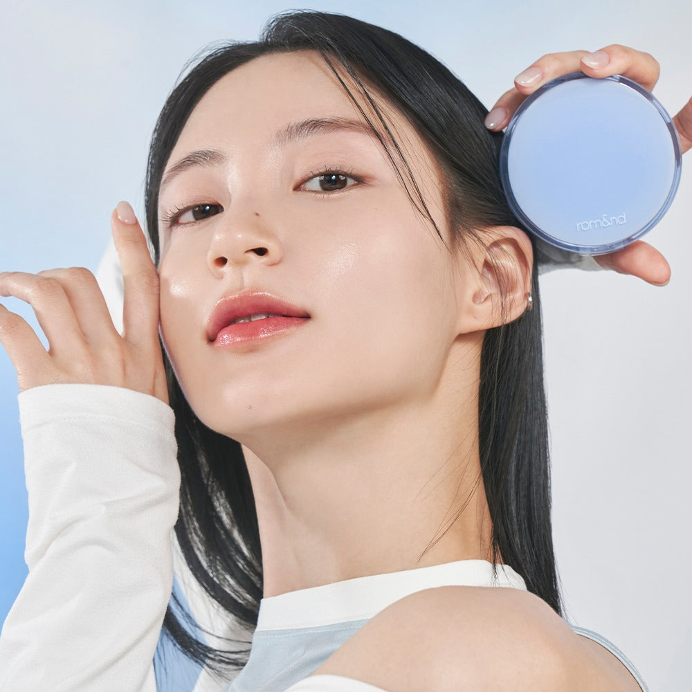 Model holding ROMAND bare water cushion in hand, showcasing fresh and natural skin look with compact design.