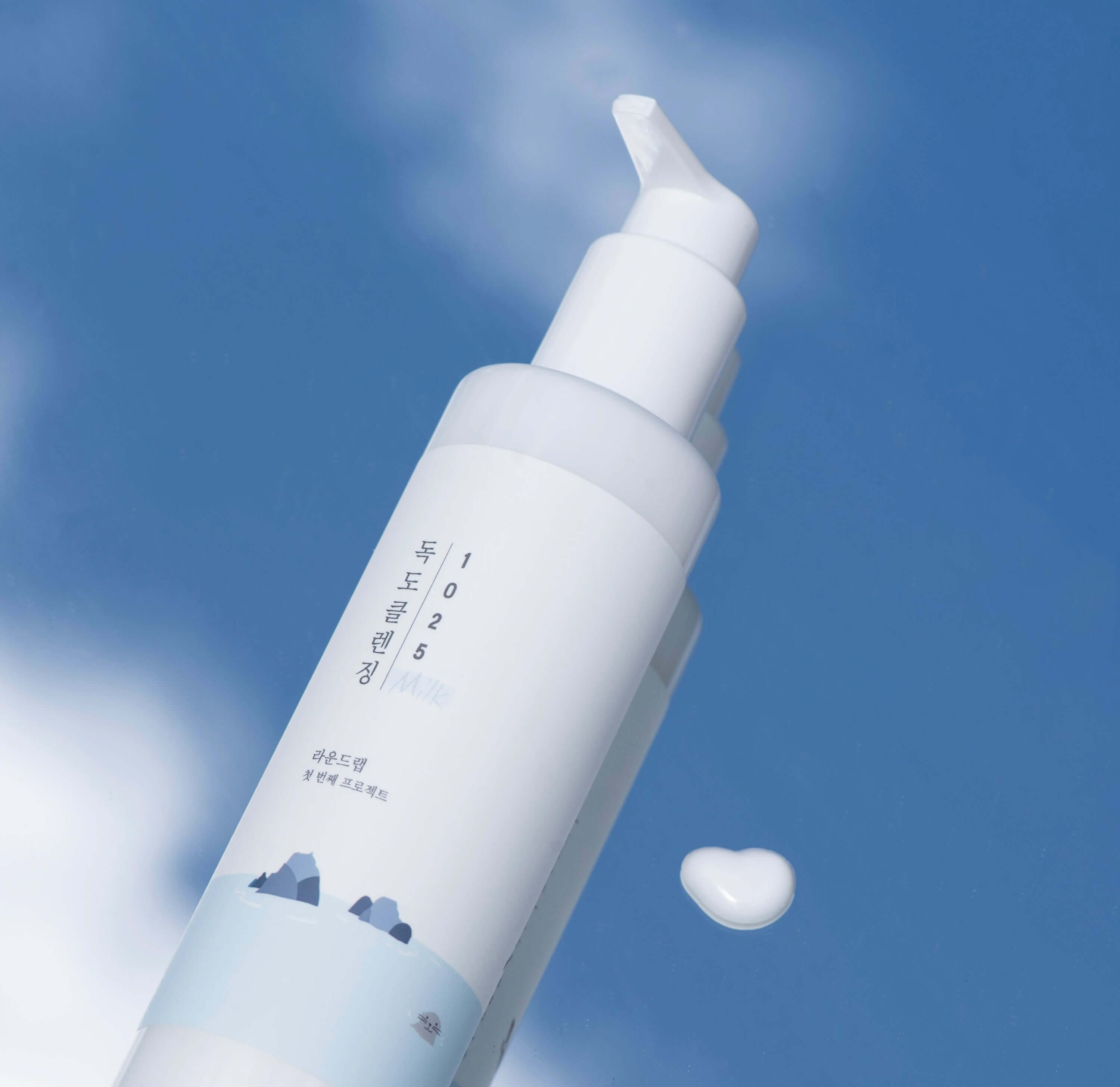Bottle of ROUND LAB 1025 Dokdo Cleansing Milk 200ml against a blue sky background.