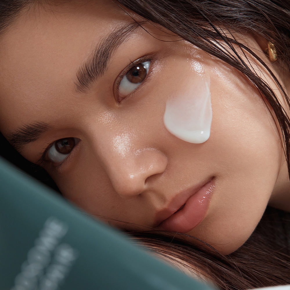 Close-up of a woman applying SHAISHAISHAI Liposome Repair Milky Cream 50ml to her cheek for skincare routine.