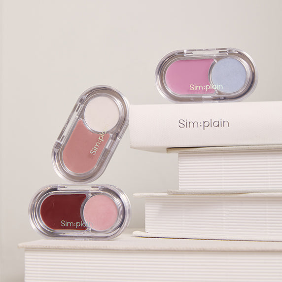 SIM;PLAIN Glim on the night makeup palette in pink and blue shades on a stack of white books.