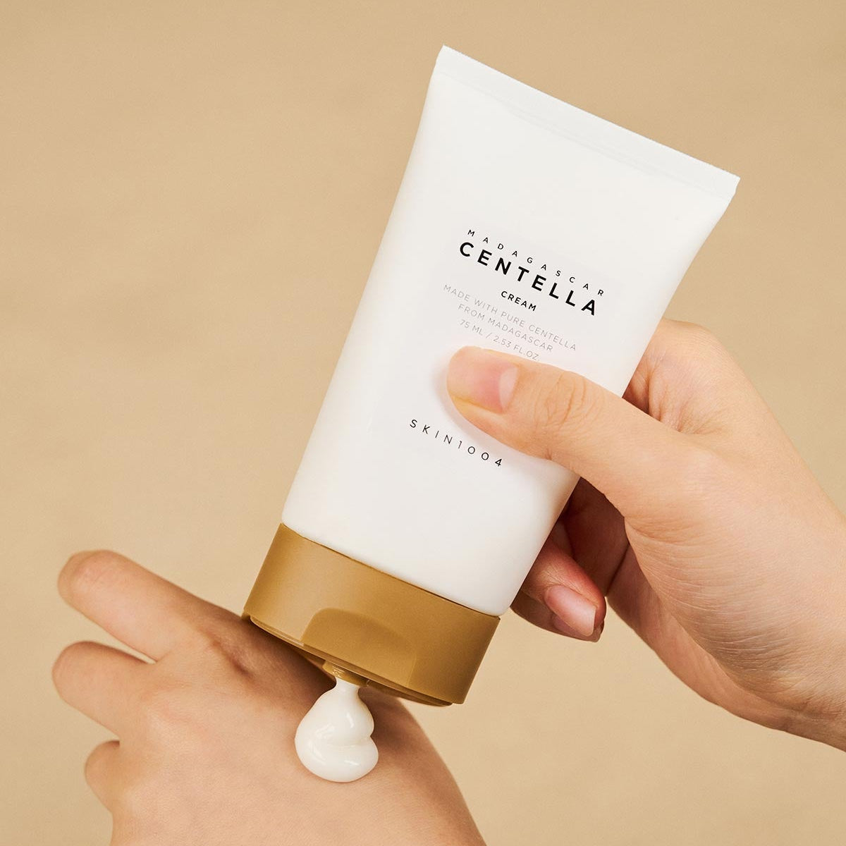 Person applying SKIN1004 Madagascar Centella Cream 75ml to hand, showcasing skincare product in use.
