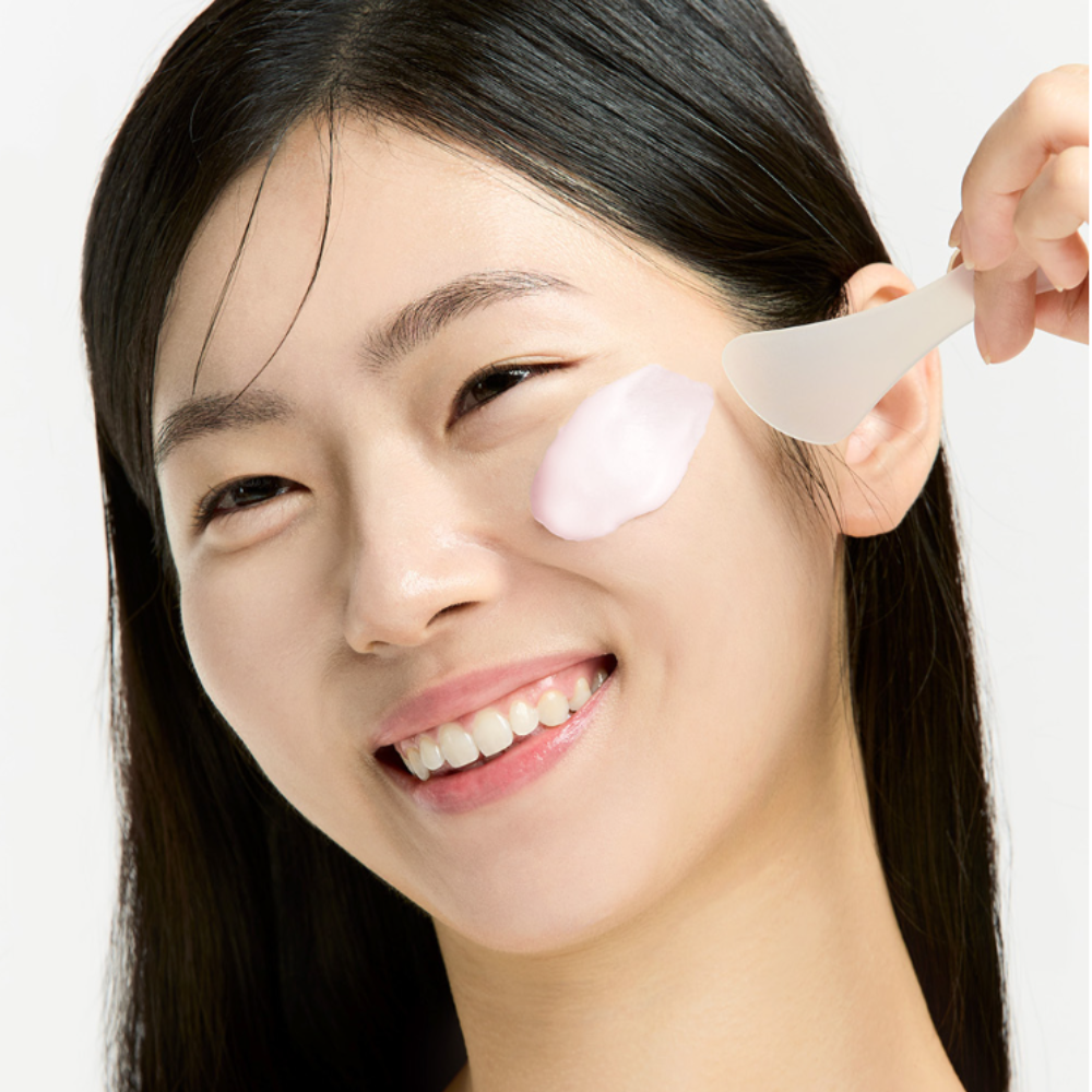 Woman applying SUNGBOON EDITOR Boosting Modeling Pack Apple Peel Glow Soothing to her face with a spatula, demonstrating skincare routine.