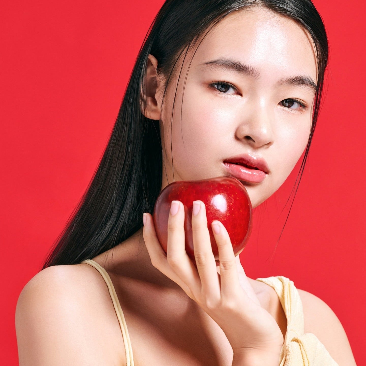 Woman holding an apple next to her face in front of a red background, promoting TOCOBO Apple Dewy Fit Cushion.