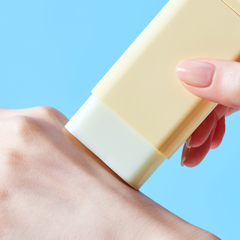 Applying TOCOBO Vita Waterproof Sun Stick on skin with a blue background.