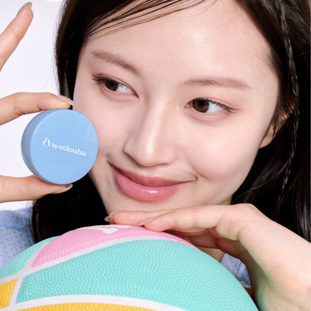 Smiling woman holding UNLEASHIA Be Be Blue Cushion beside her face, demonstrating smooth coverage and radiant skin