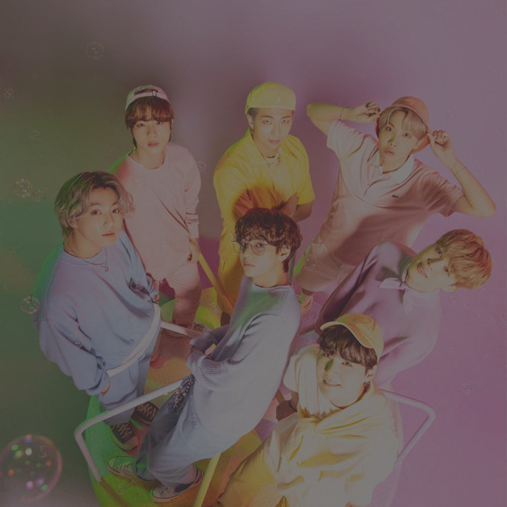 Group of seven people posing in colorful outfits with bubbles in a vibrant setting.