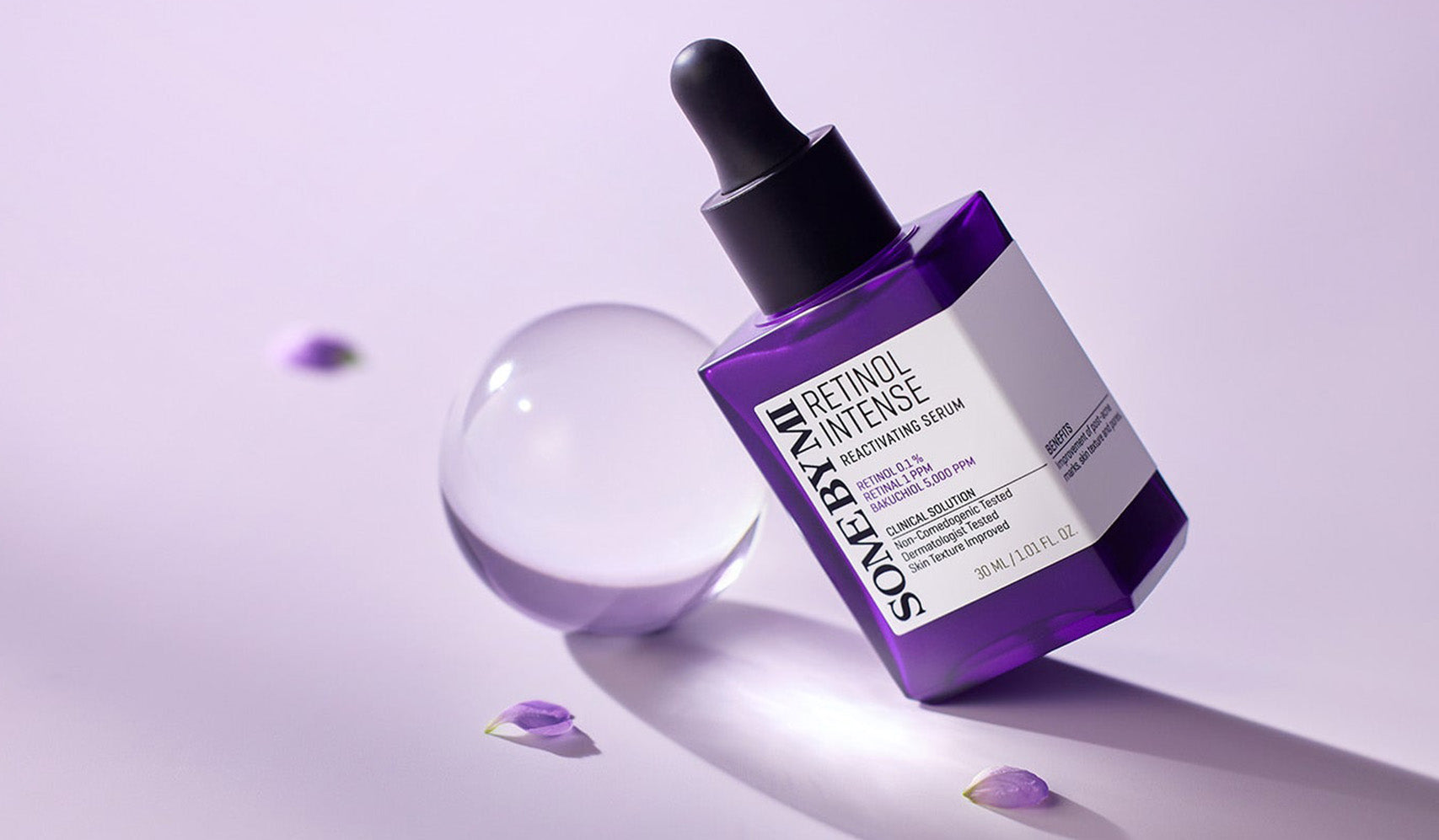 Purple retinol serum bottle with dropper on a soft purple background and petals.