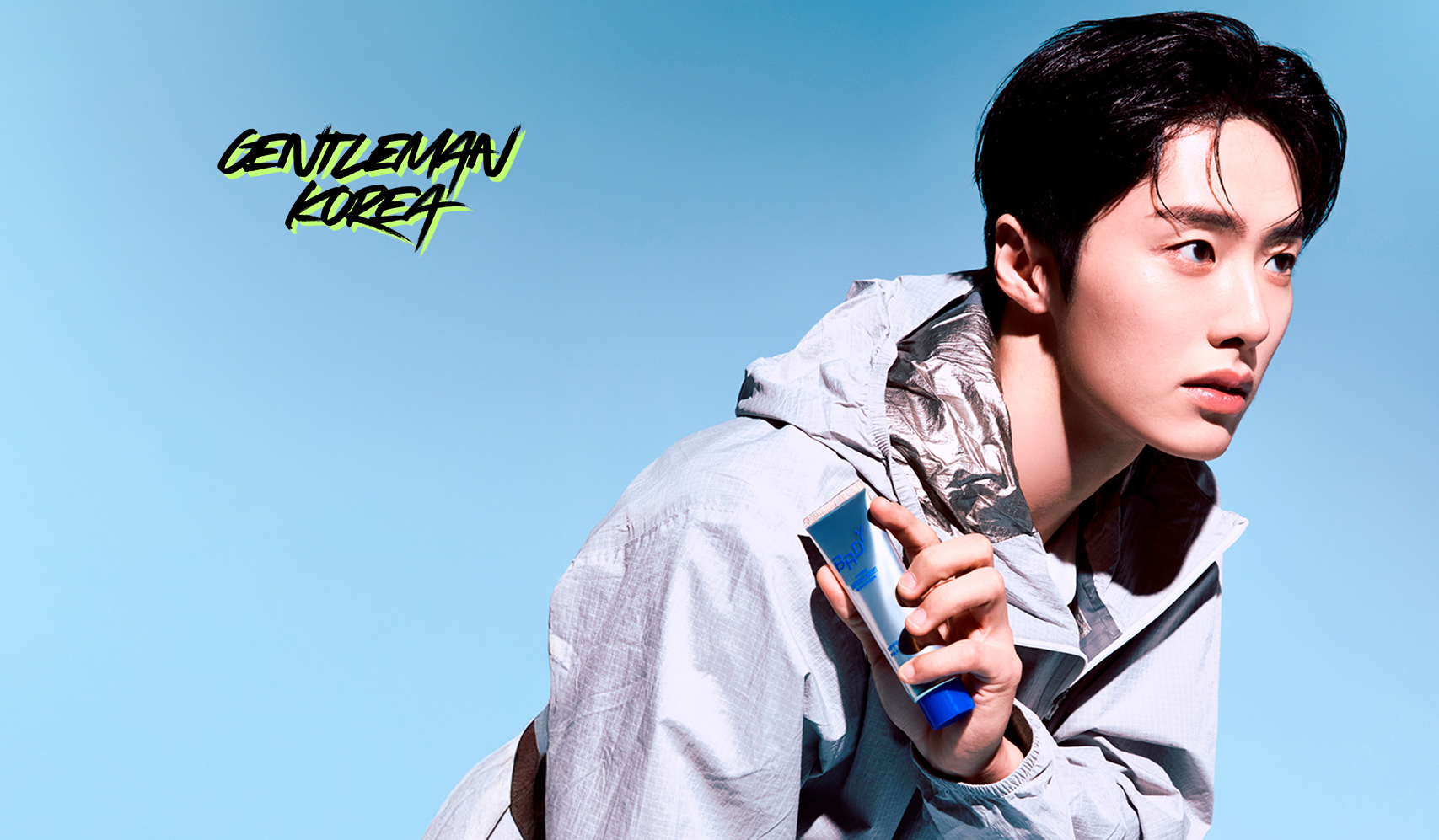 Person in a stylish jacket holding a smartphone against a blue background with 'Gentleman Korea' text.