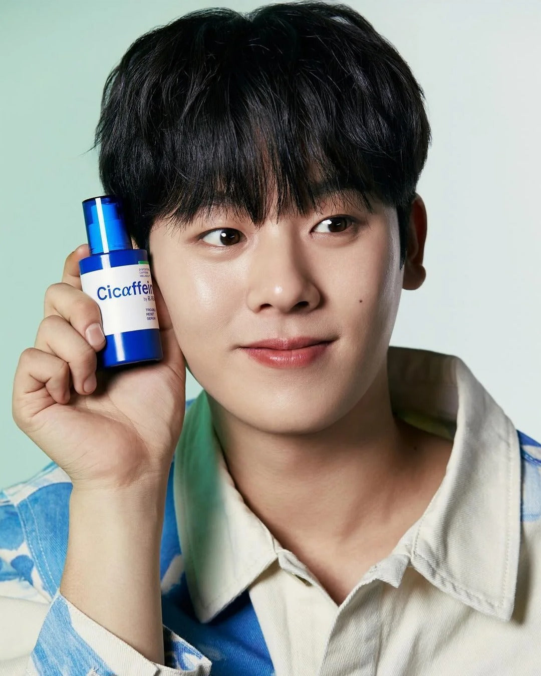 Person holding a blue Cicaffel product bottle close to their face, wearing a white and blue shirt.