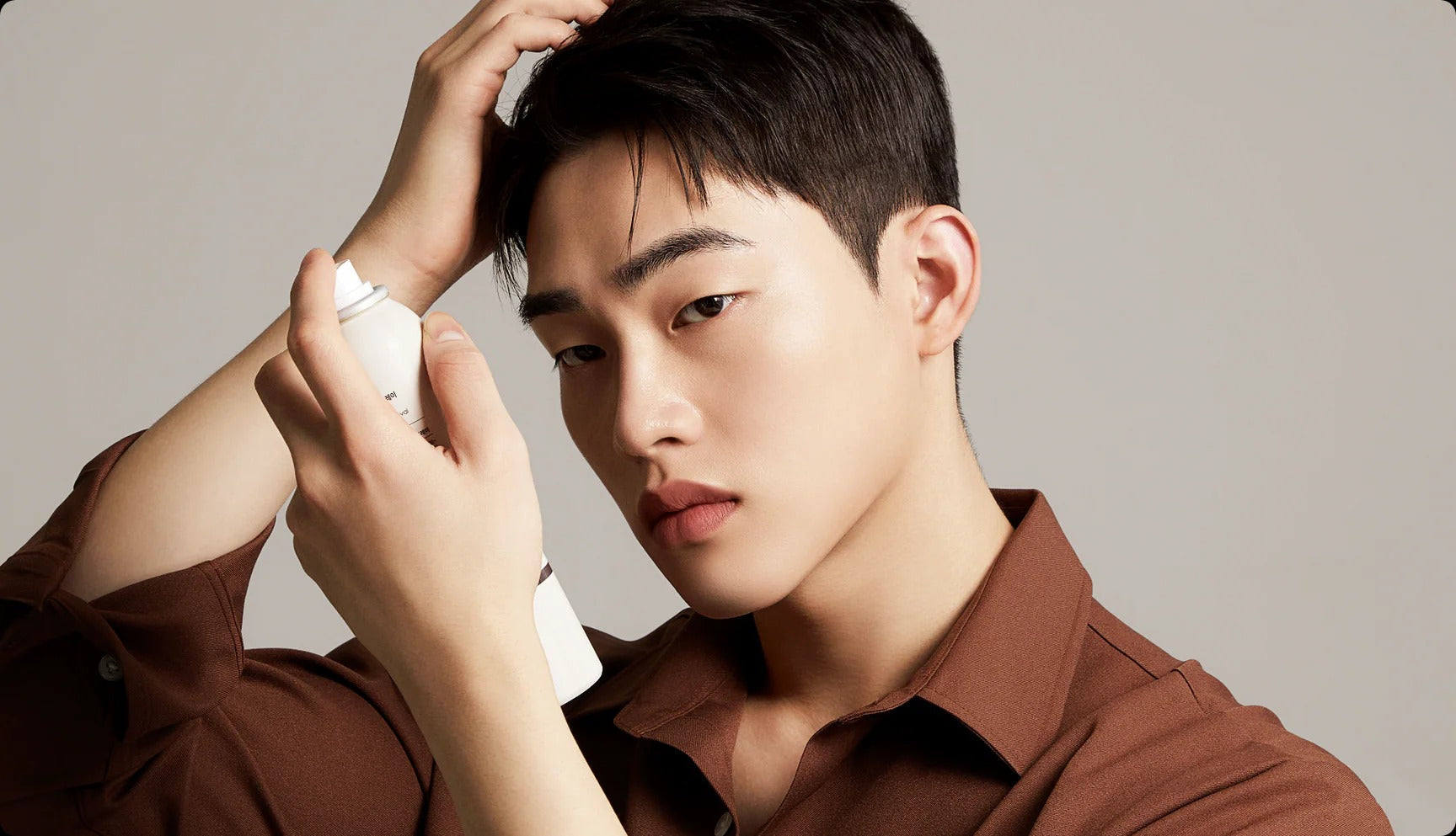 Man styling hair with hair product, wearing a brown shirt.