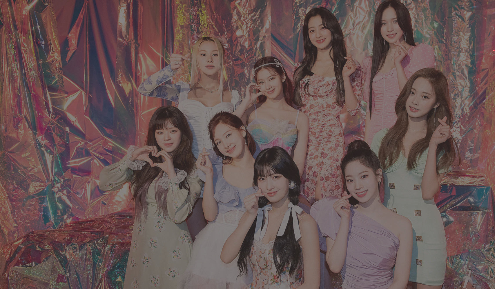 Group of women in colorful outfits with heart gestures against a vibrant, iridescent background.