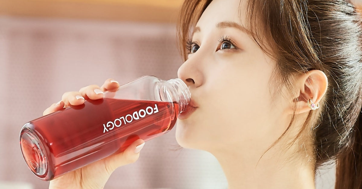 Person enjoying a red beverage from a bottle labeled Foodology: The Tasty Science of Good Eats and Healthy Treats!