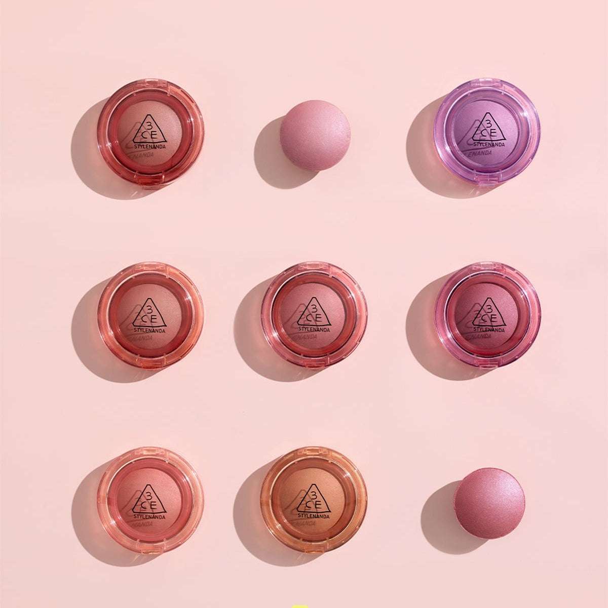 Assorted 3CE Bouncy Blur Balm compacts in various shades on a pink background, highlighting makeup products.