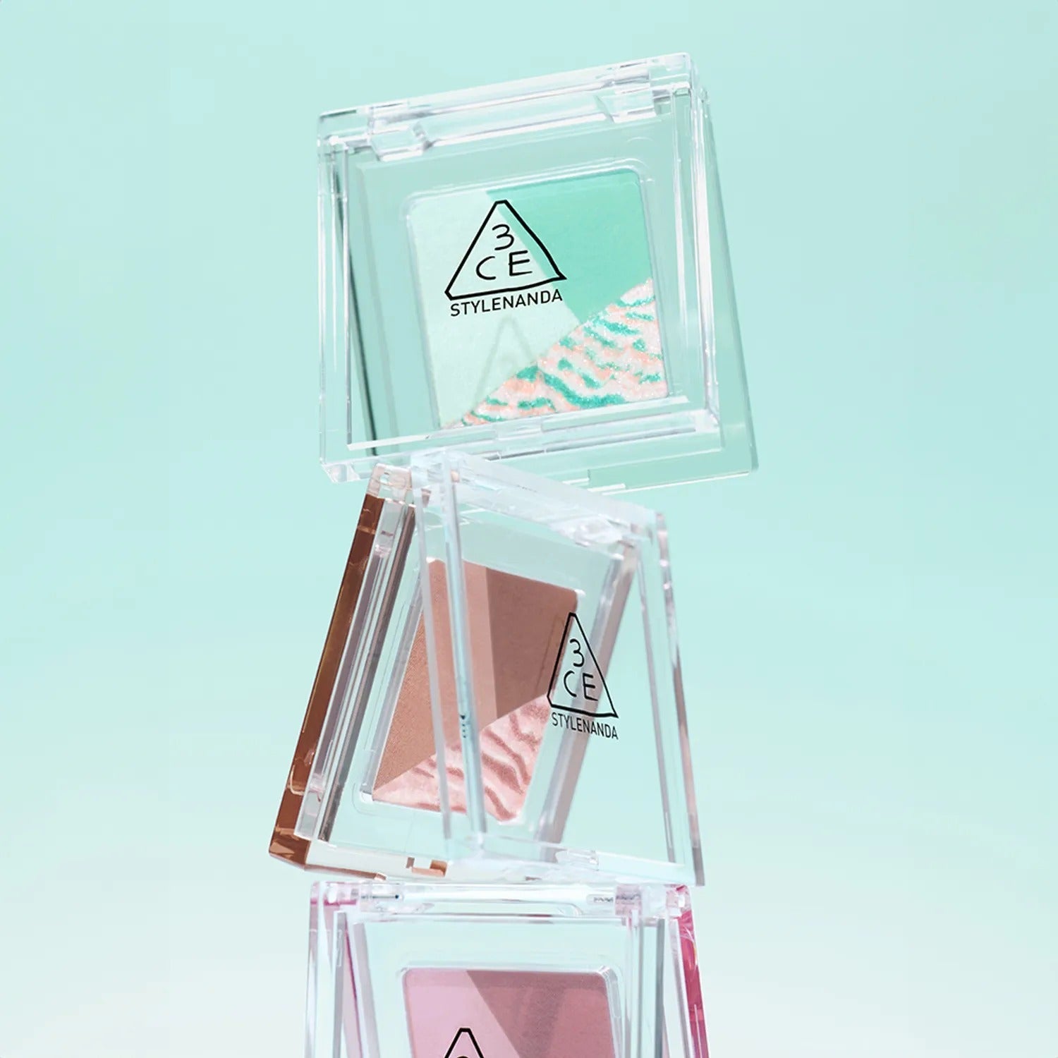 Stack of 3CE Color Grid Eyeshadow palettes with various shades on a light green background