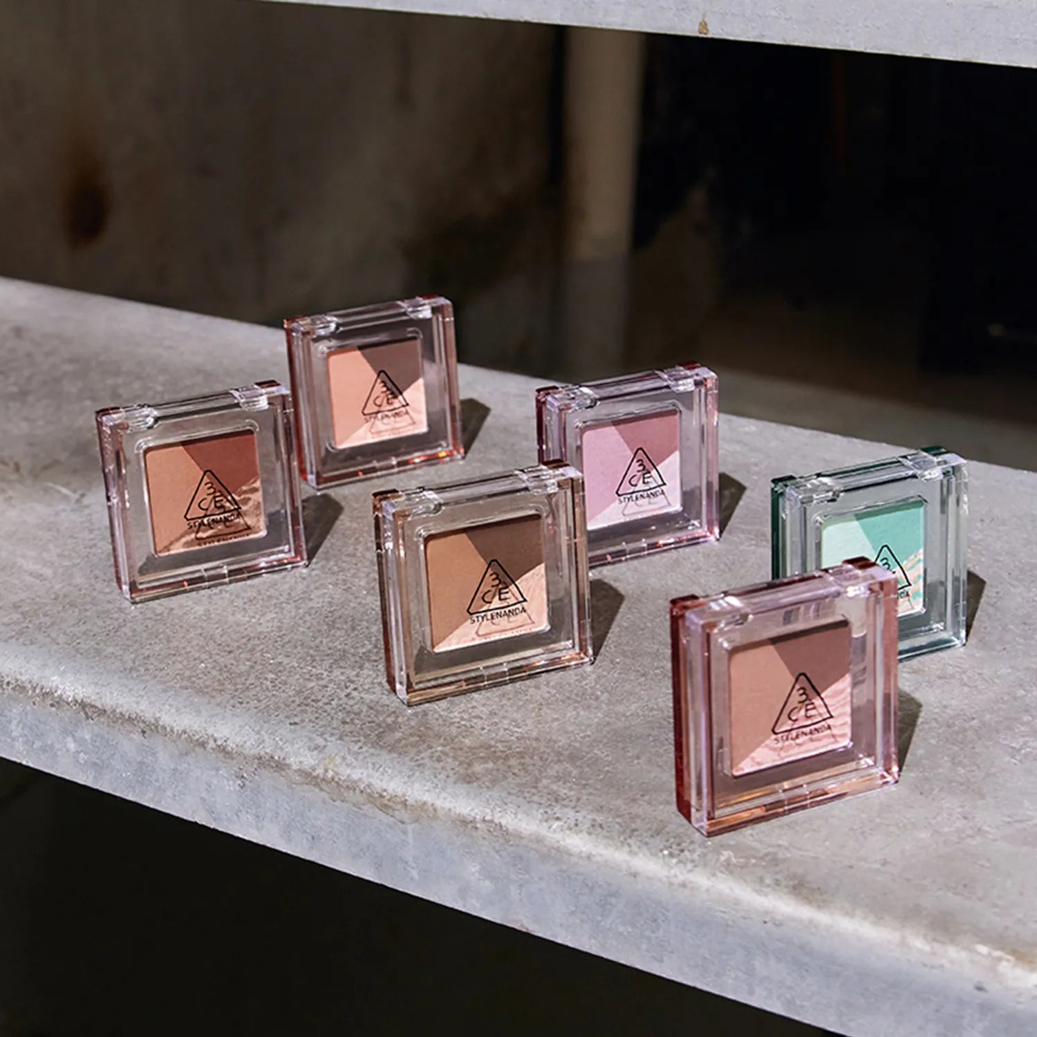 Six 3CE Color Grid Eyeshadow palettes displayed on a stone surface showcasing various shades.