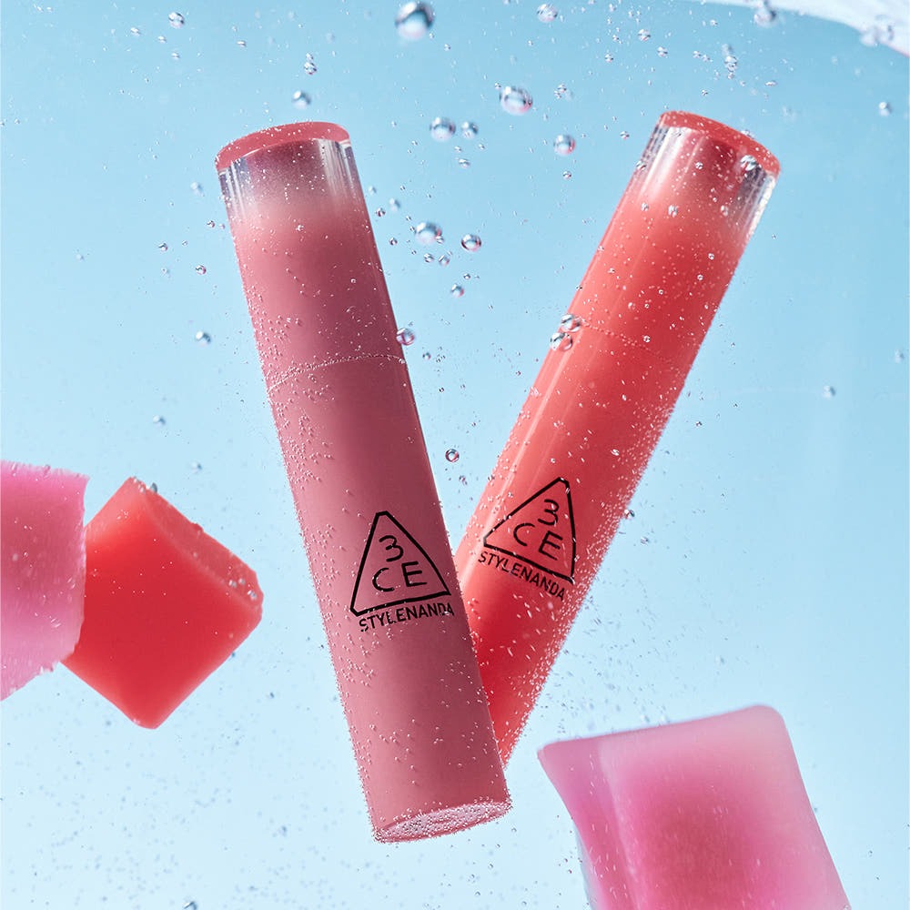 Two 3CE Lazy Pop Lip Stain tubes submerged in water, showcasing vibrant color and sleek packaging.
