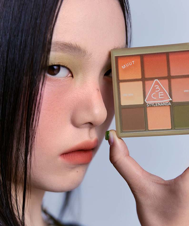 Woman holding 3CE Multi Eye Color Palette 7g with orange and green tones