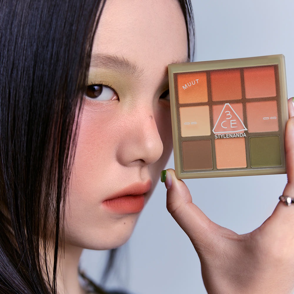 Woman holding 3CE Multi Eye Color Palette 7g with orange and green tones