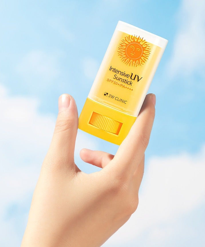 Hand holding 3W CLINIC Intensive UV Sun Sticks 20g against a blue sky background.