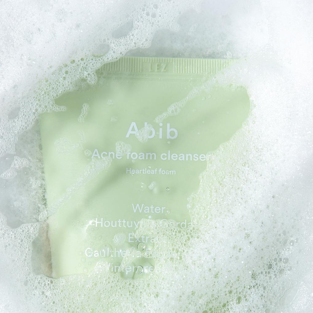 ABIB Acne Foam Cleanser with Mugwort Foam 250ml in a green tube covered in white foam, showcasing its cleansing properties.