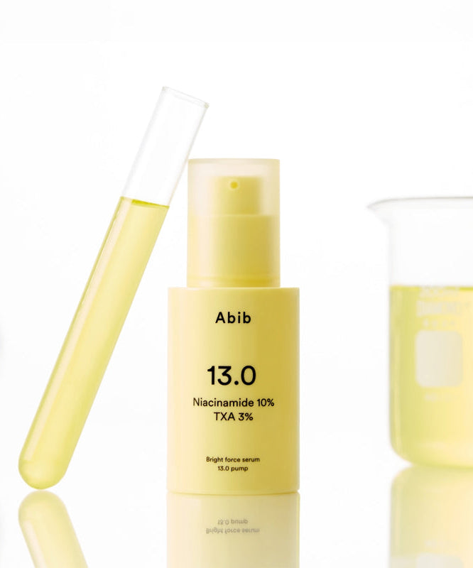 ABIB Bright Force Serum 13.0 Pump 30ml bottle with a yellow liquid in a test tube and beaker in the background.