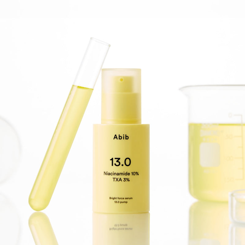 ABIB Bright Force Serum 13.0 Pump 30ml bottle with a yellow liquid in a test tube and beaker in the background.