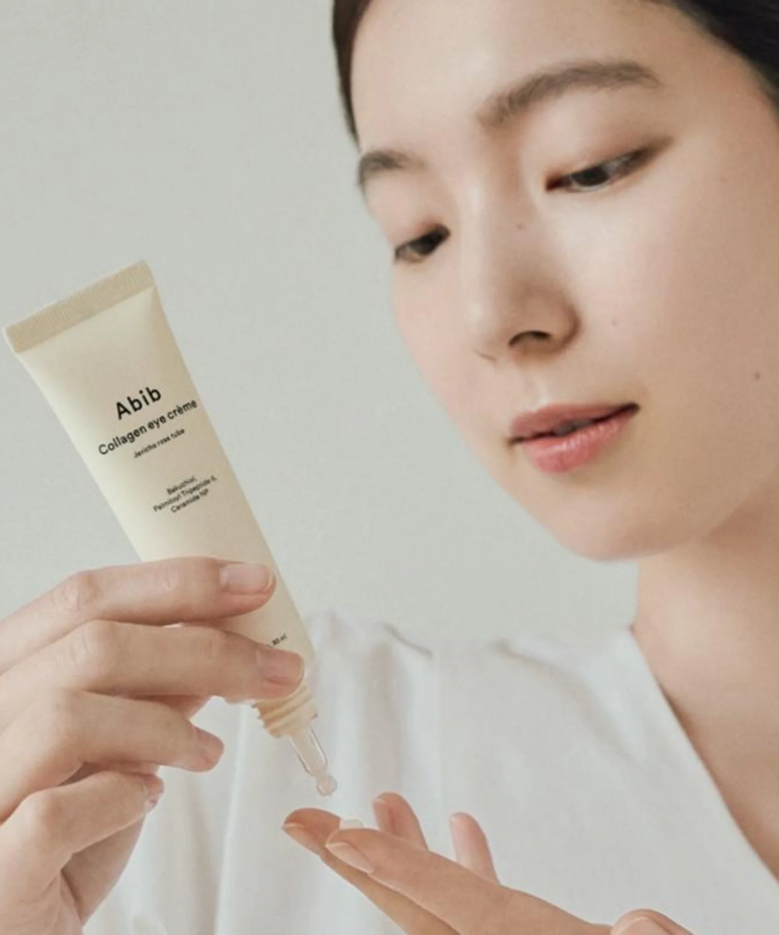 Woman holding ABIB Collagen Eye Cream Jericho Rose Tube 30ml applying cream to fingers.