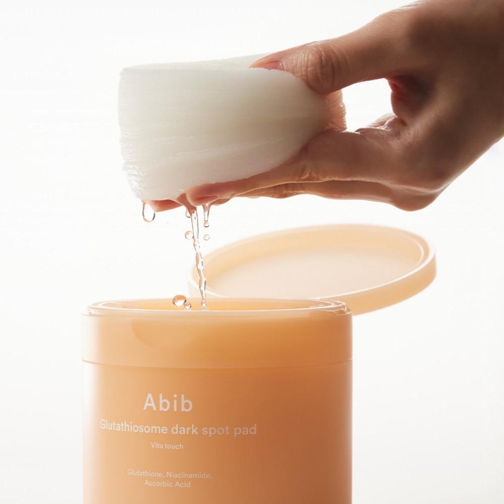ABIB Glutathiosome Dark Spot Pad Vita Touch 60 EA, showing hand holding a pad above container, with product details visible.