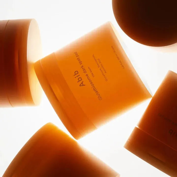 ABIB Glutathiosome Dark Spot Pad Vita Touch 60 EA skincare containers in warm lighting, highlighting product design and branding.