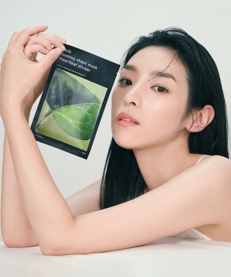 Woman holding ABIB Gummy Sheet Mask Heartleaf Sticker 10 sheets, showcasing skincare product packaging.