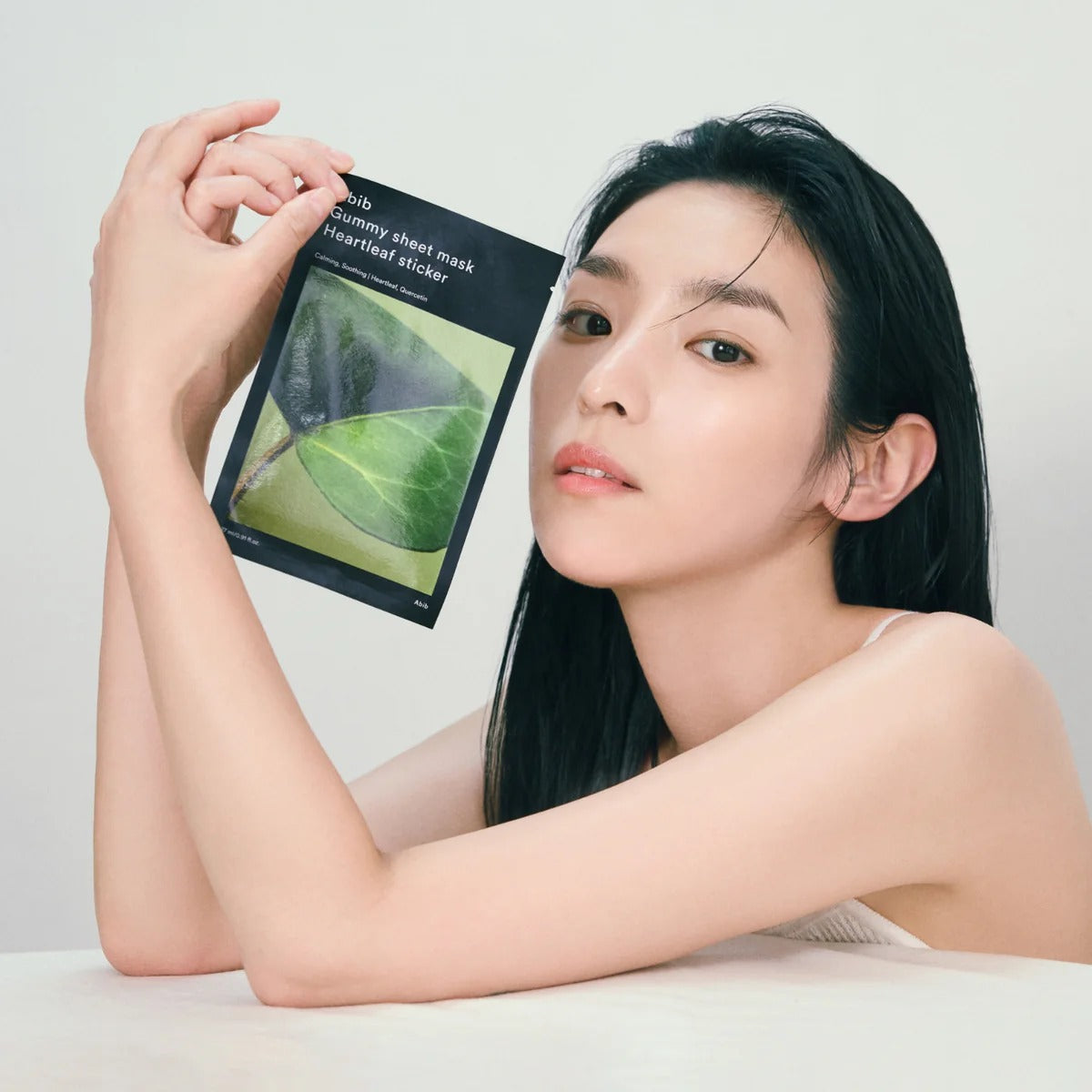 Woman holding ABIB Gummy Sheet Mask Heartleaf Sticker 10 sheets, showcasing skincare product packaging.
