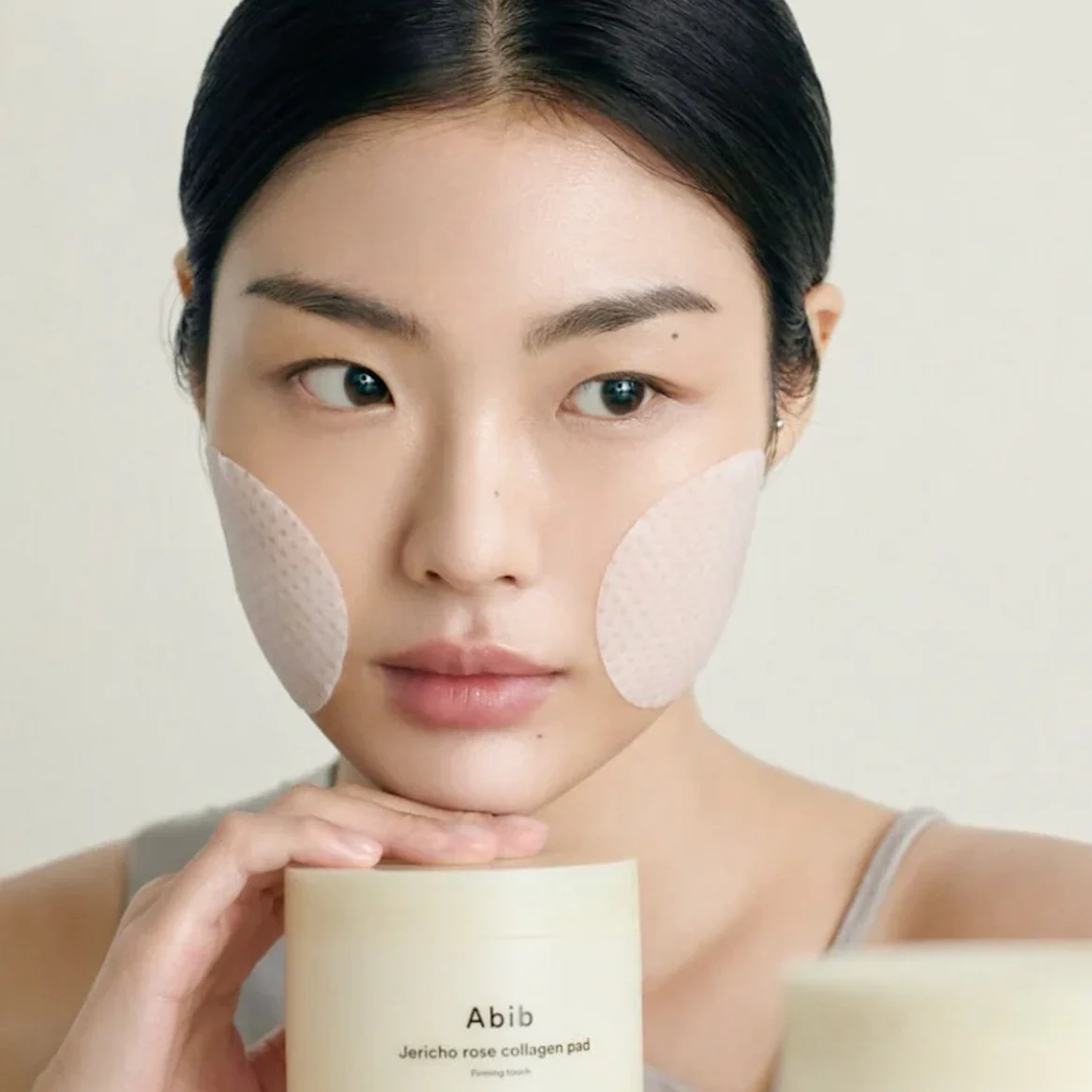 Woman using ABIB Jericho Rose Collagen Pad Firming Touch 60 Pads for skincare routine.
